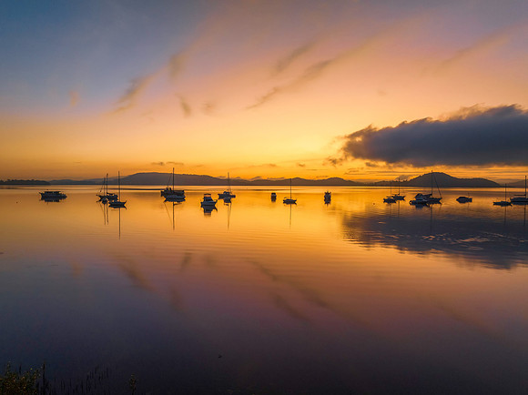 Sunrise over the water with fog, boats, clouds and reflections