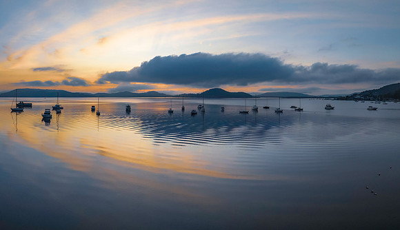 Sunrise over the water with fog, boats, clouds and reflections