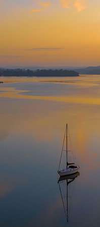 Sunrise over the water in soft orange and blue with sailboat