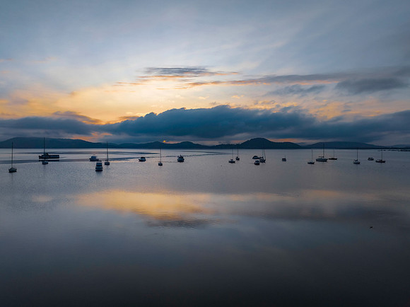 Sunrise over the water with fog, boats, clouds and reflections