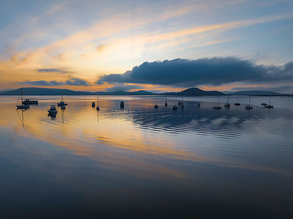 Sunrise over the water with fog, boats, clouds and reflections