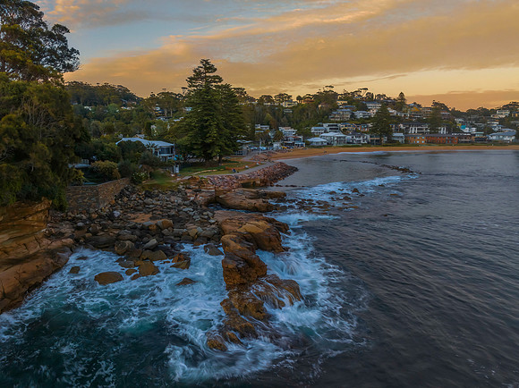 Sunrise over the ocean with rocks and coastal suburb