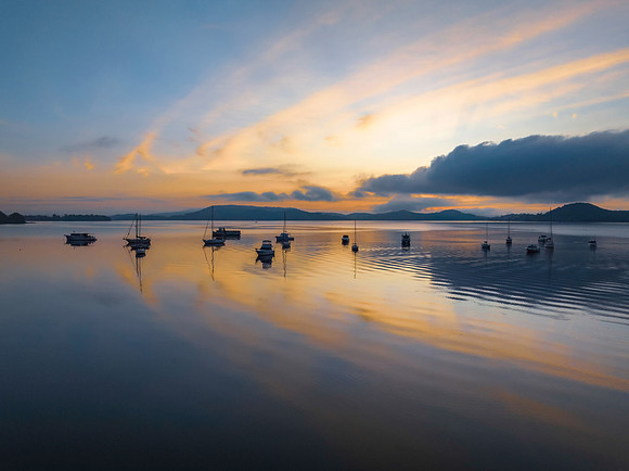 Sunrise over the water with fog, boats, clouds and reflections