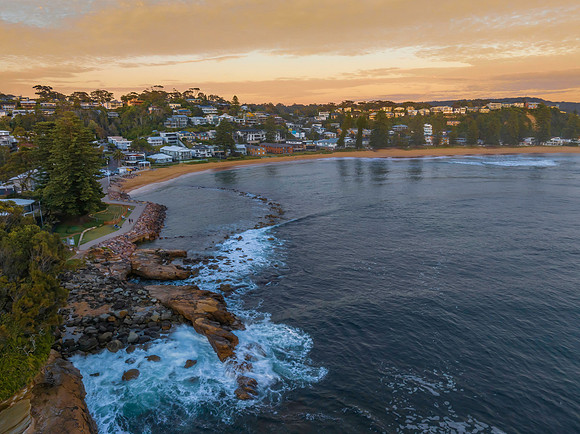 Sunrise over the ocean with rocks and coastal suburb
