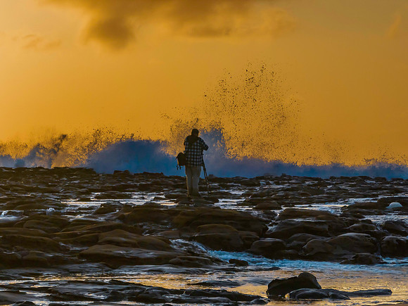 Photographer capturing the sunrise and splashes from the rock pl