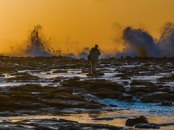 Photographer capturing the sunrise and splashes from the rock pl