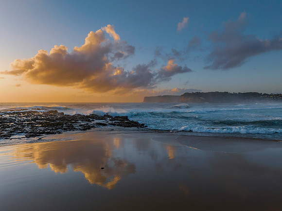 Surfs up at the beach with scattered clouds and reflections