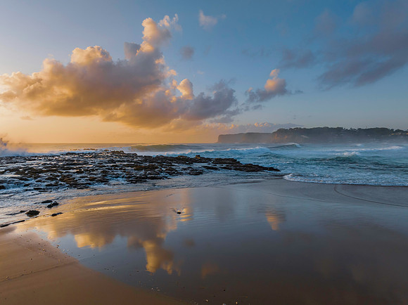 Surfs up at the beach with scattered clouds and reflections