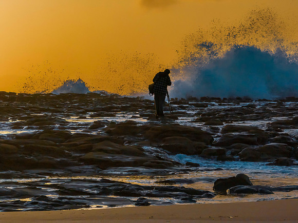 Photographer capturing the sunrise and splashes from the rock pl