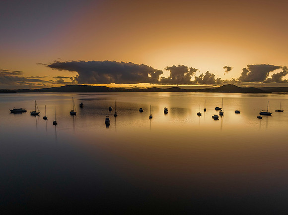 Aerial sunrise waterscape with boats and clouds in soft gold