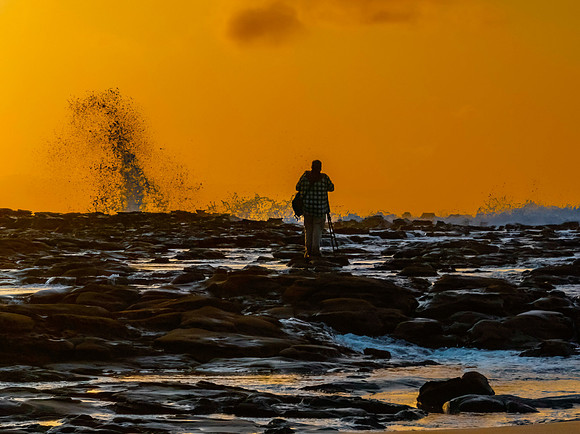 Photographer capturing the sunrise and splashes from the rock pl