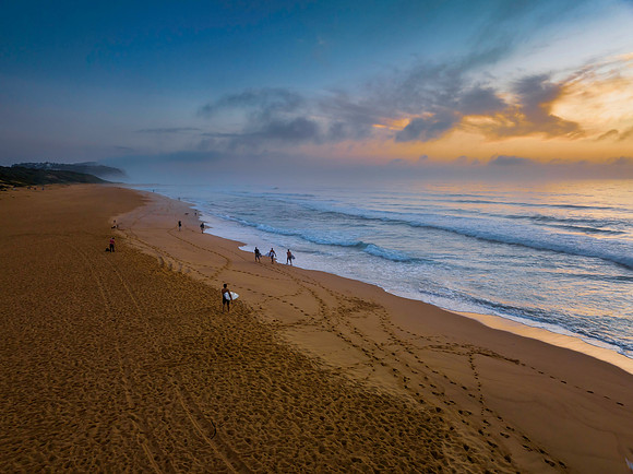 Hazy Summer sunrise at the seaside with surfers and photographer