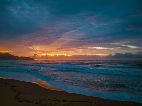Cloud covered sunrise at the seaside in pink and blue