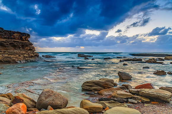 Moody sunrise seascape with clouds at the rocky inlet