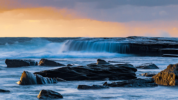 Moody sunrise seascape with clouds at the rocky inlet