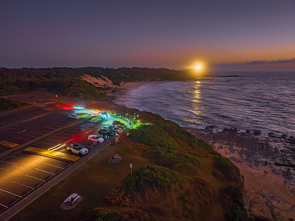 Aerial dawn seascape with car lights, lighthouse, high tide and