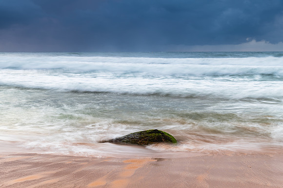 Sunrise at the seaside with rocks and rain clouds