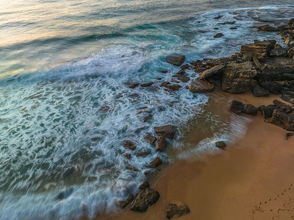 Top down sunrise at the seaside with rocks, waves and swirls