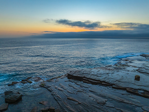 Sunrise seascape and rocky Inlet with thick fog cloud over the o