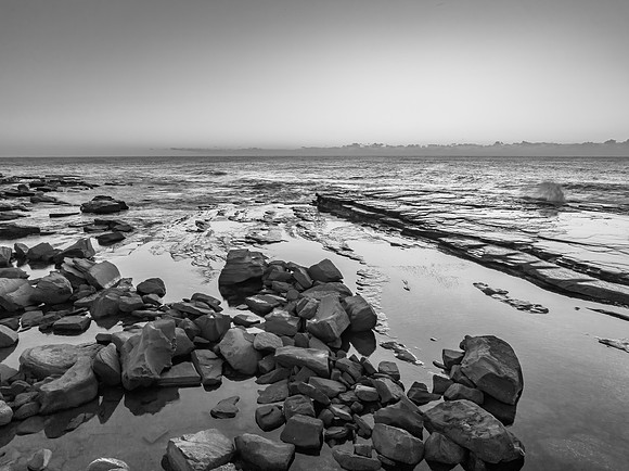 Monochrome sunrise over the sea and rocky Inlet with clear skies