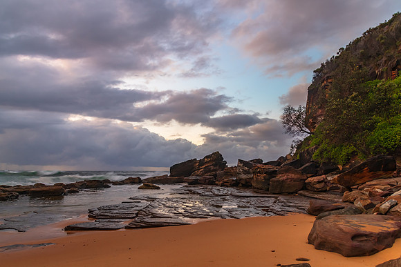Sunrise at the seaside with rocks and rain clouds