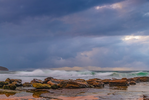 Sunrise at the seaside with rocks and rain clouds