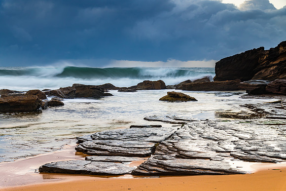 Sunrise at the seaside with rocks and rain clouds