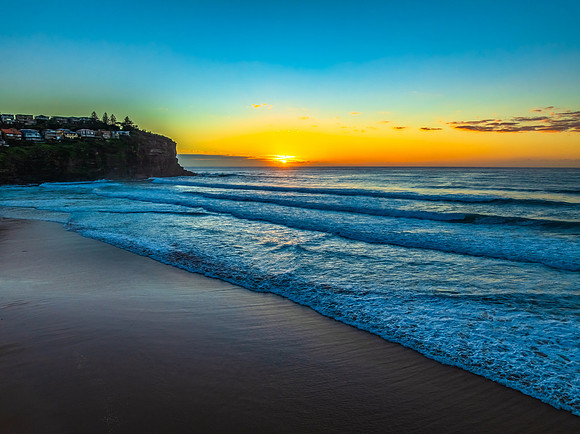 Sunrise at the beach with waves and a smattering of clouds