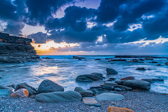 Moody sunrise seascape with clouds at the rocky inlet