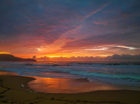 Cloud covered sunrise at the seaside in pink and blue