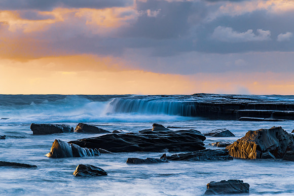 Moody sunrise seascape with clouds at the rocky inlet