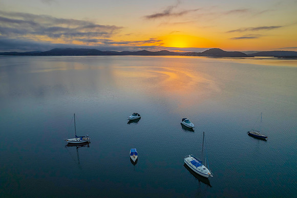Sunrise waterscape with boats, soft clouds and reflections