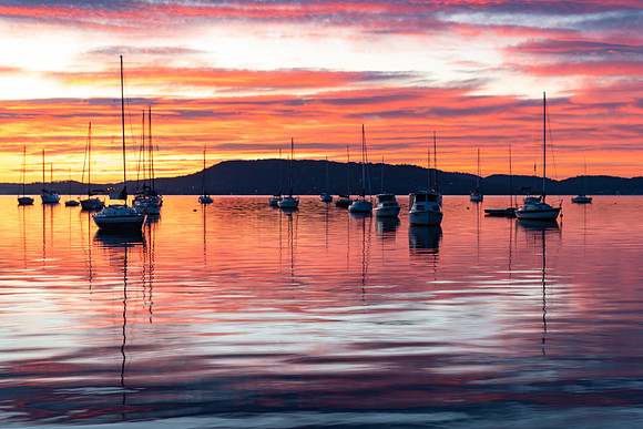 Sunrise over the water with boats, reflections and high cloud