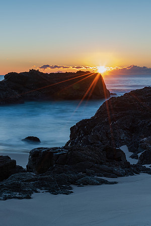 Sunrise seascape, rocky beach and sun rays