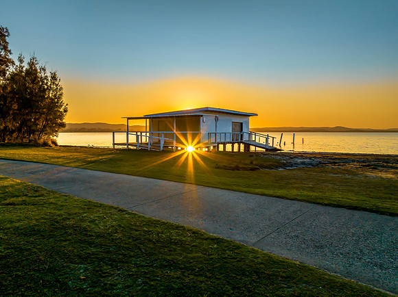 Sunset over the lake with boathouse and sun starburst