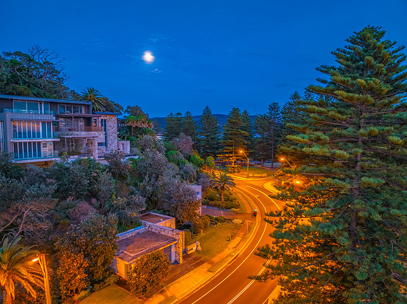 Sunrise coastal scenery with moon, trees, road and a house