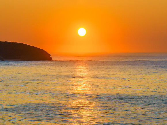 Soft sunrise seascape with full sun in a hazy cloudless sky