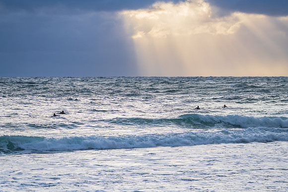 Wet weather sunrise seascape with surfers and sun rays on the ho