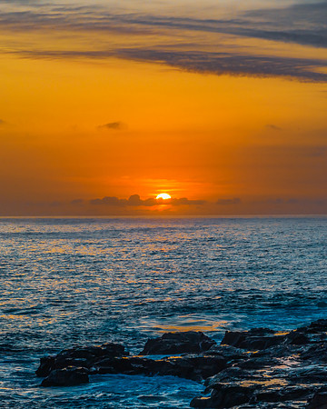 Sunrise over the calm ocean with light cloud and rocks