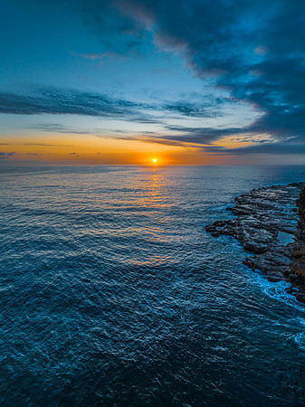 Sunrise over the calm ocean with light cloud and rocks