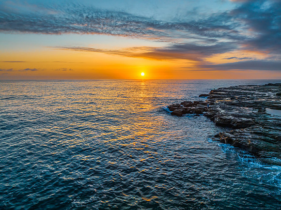 Sunrise over the calm ocean with light cloud and rocks