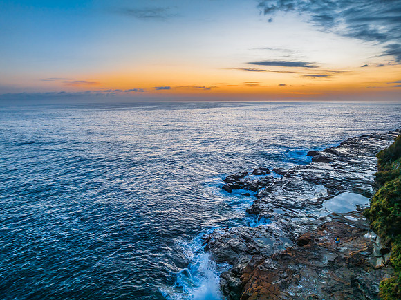 Sunrise over the calm ocean with light cloud and rocks