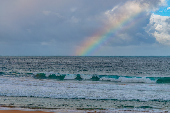Rainbow over the ocean with waves and clouds in the sky