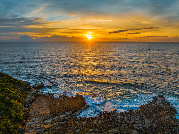 Sunrise over the sea and rock platform with high cloud