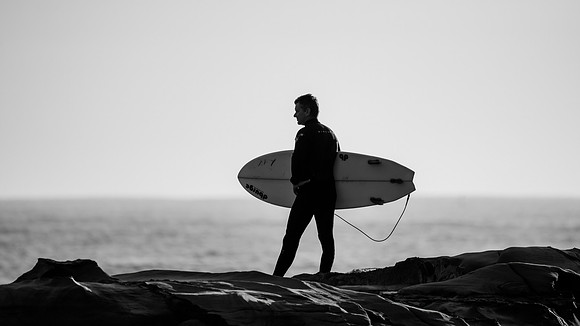Surfer in silhouette on rock ledge