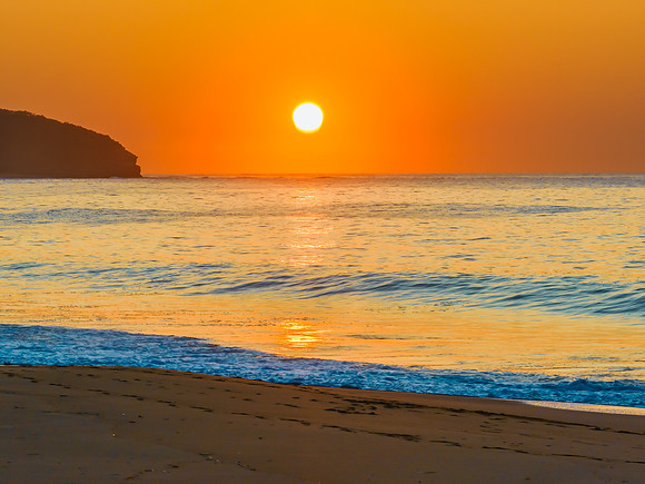 Soft sunrise seascape with full sun in a hazy cloudless sky