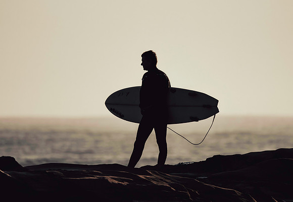 Surfer in silhouette on rock ledge