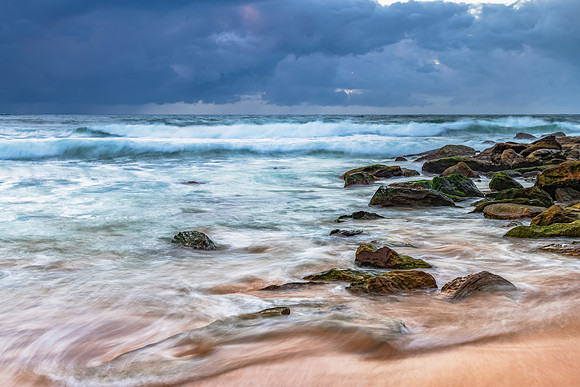 Sunrise at the seaside with rocks and rain clouds