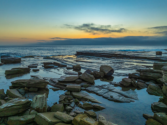 Sunrise seascape and rocky Inlet with thick fog cloud over the o