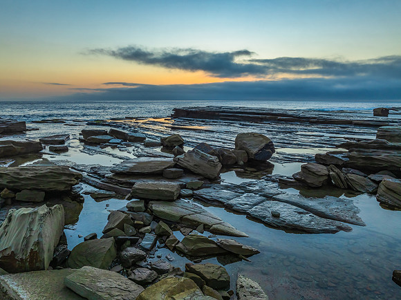 Sunrise seascape and rocky Inlet with thick fog cloud over the o